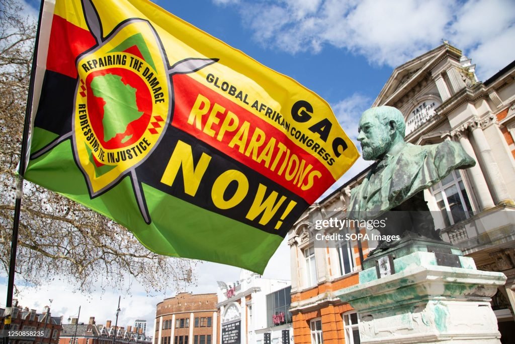 A man holds a flag calling for reparations in Windrush square during the commemoration.. Fifth anniversary of remembering those who have been impacted by the Windrush scandal which saw people from the Caribbean treated like illegal immigrants by the Home Office despite arriving in Britain legally.